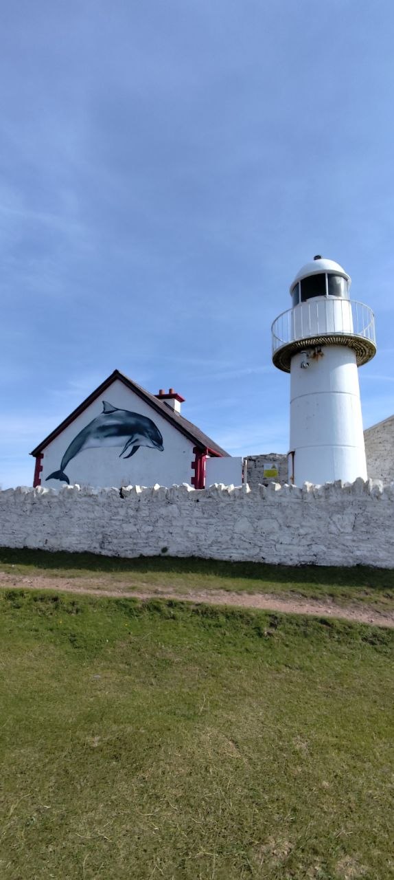 Faro blanco de Dingle junto a una casa con un gran mural del delfín Fungie pintado en la pared