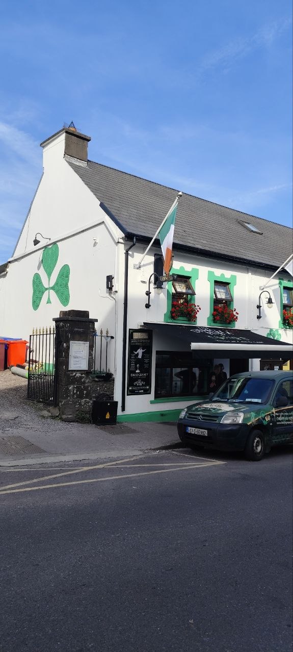 Pub tradicional de Dingle con mural de trébol y una furgoneta verde aparcada al frente