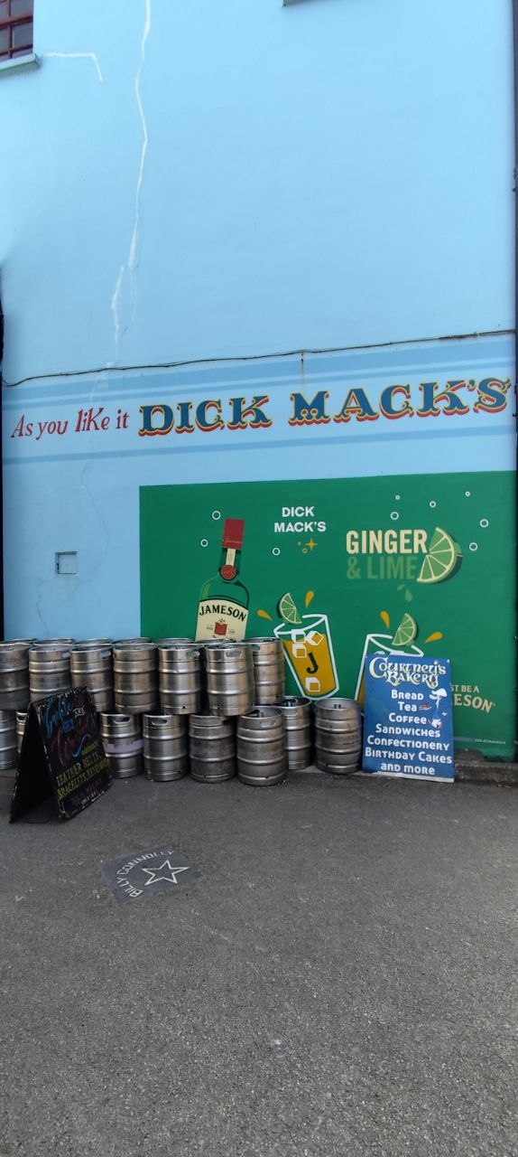 Fachada azul del famoso pub Dick Mack's en Dingle, con barriles de cerveza y un cartel de Courtney's Bakery