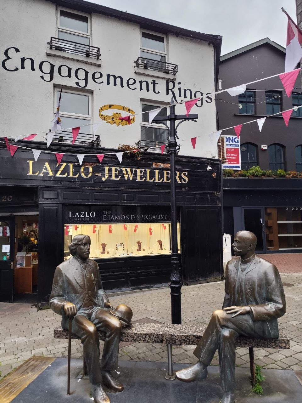 Dos estatuas de bronce sentadas en un banco en una calle de Galway