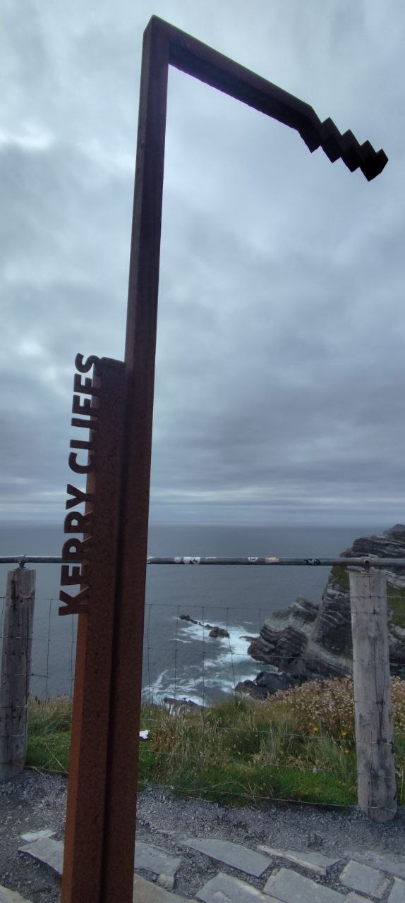 Cartel de madera de los Kerry Cliffs sobre un acantilado, con el mar Atlántico de fondo