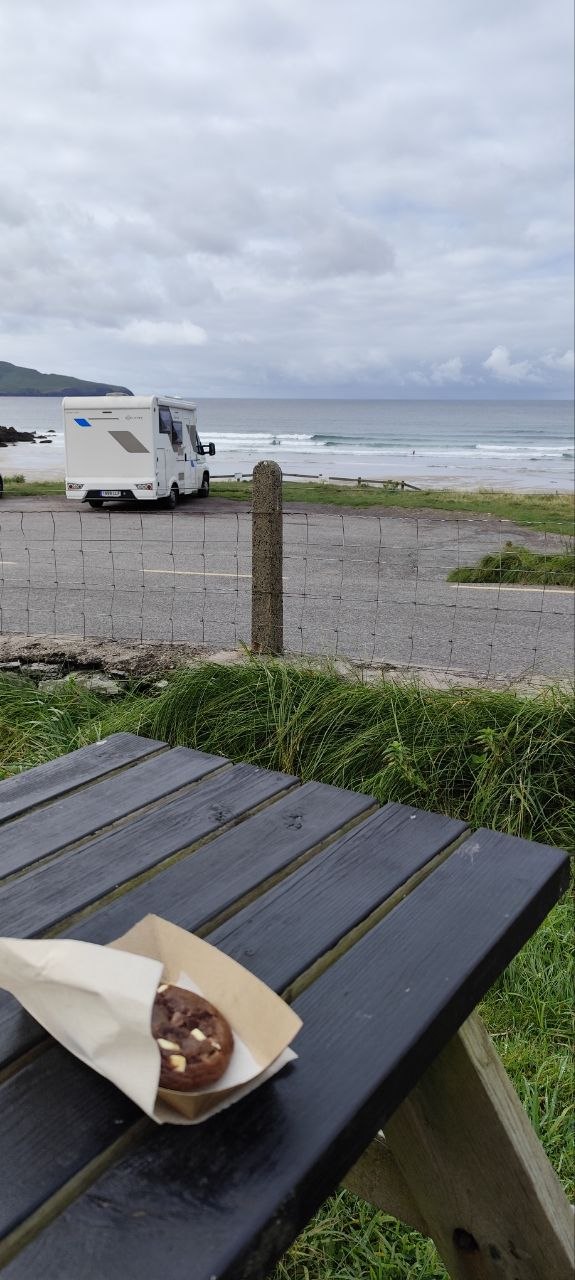 Pausa de mediodía en un mirador del Ring of Kerry: galleta de chocolate en la mesa de madera, con la autocaravana y el mar de fondo