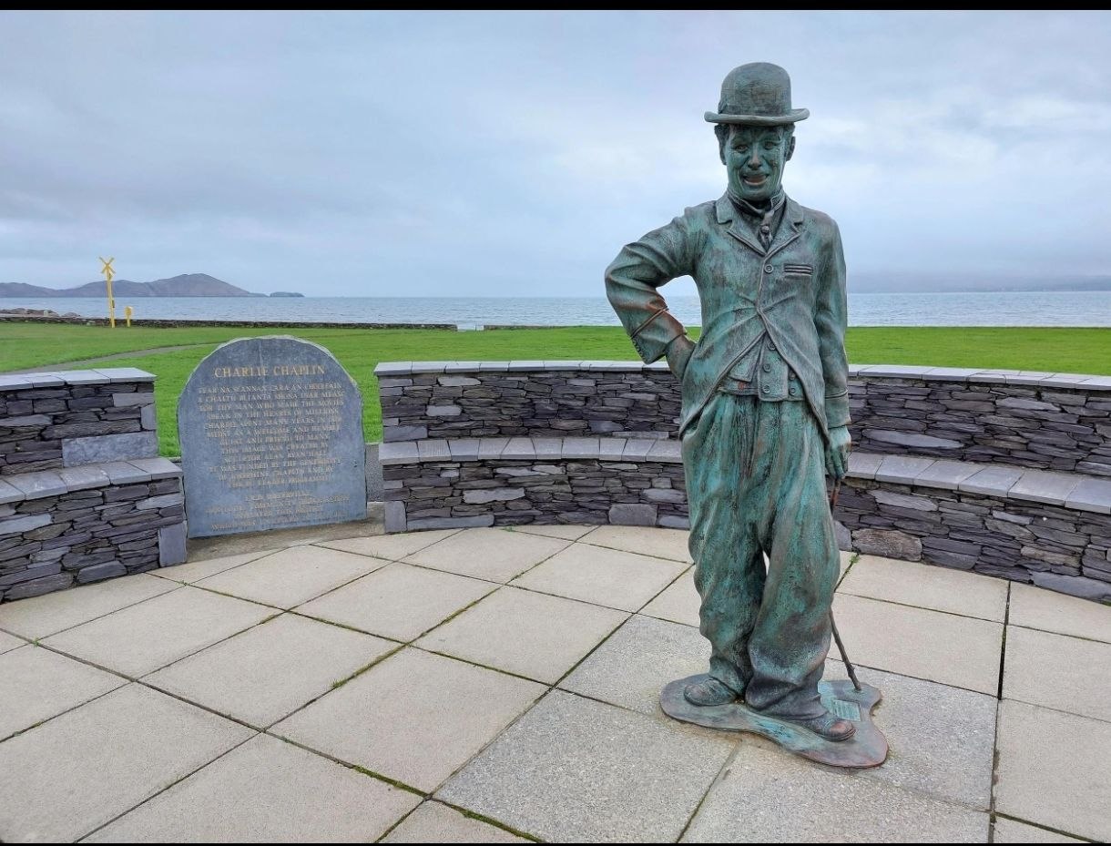 Estátua de bronce de Charlie Chaplin en el paseo marítimo de Waterville, con la bahía de fondo